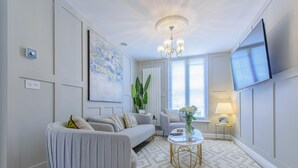 A modern living room with a grey sofa, a round armchair, a coffee table, and a TV mounted on the wall. - Ultra Modern: Luxury 1 Bed Serviced Apartment (Dunstable)