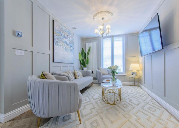 A modern living room with a grey sofa, a round armchair, a coffee table, and a TV mounted on the wall.