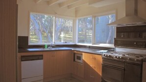 Una cocina con gabinetes de madera, lavavajillas, estufa y ventanas amplias.