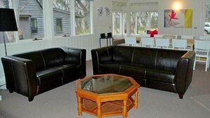 Un salón amplio con un sofá de cuero negro, una mesa de centro de vidrio y un comedor con sillas blancas y una mesa.