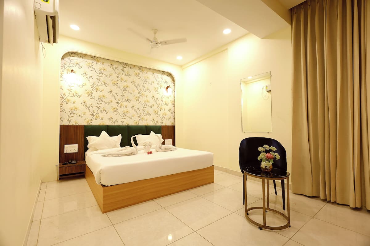 A neatly arranged hotel room with a bed, a chair, a small table with a vase, and a mirror on the wall.