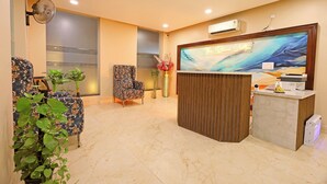 A reception area with a marble floor, two patterned chairs, a reception desk, and a wall-mounted air conditioner. - The Blue Vista Hotel (Greater Noida)