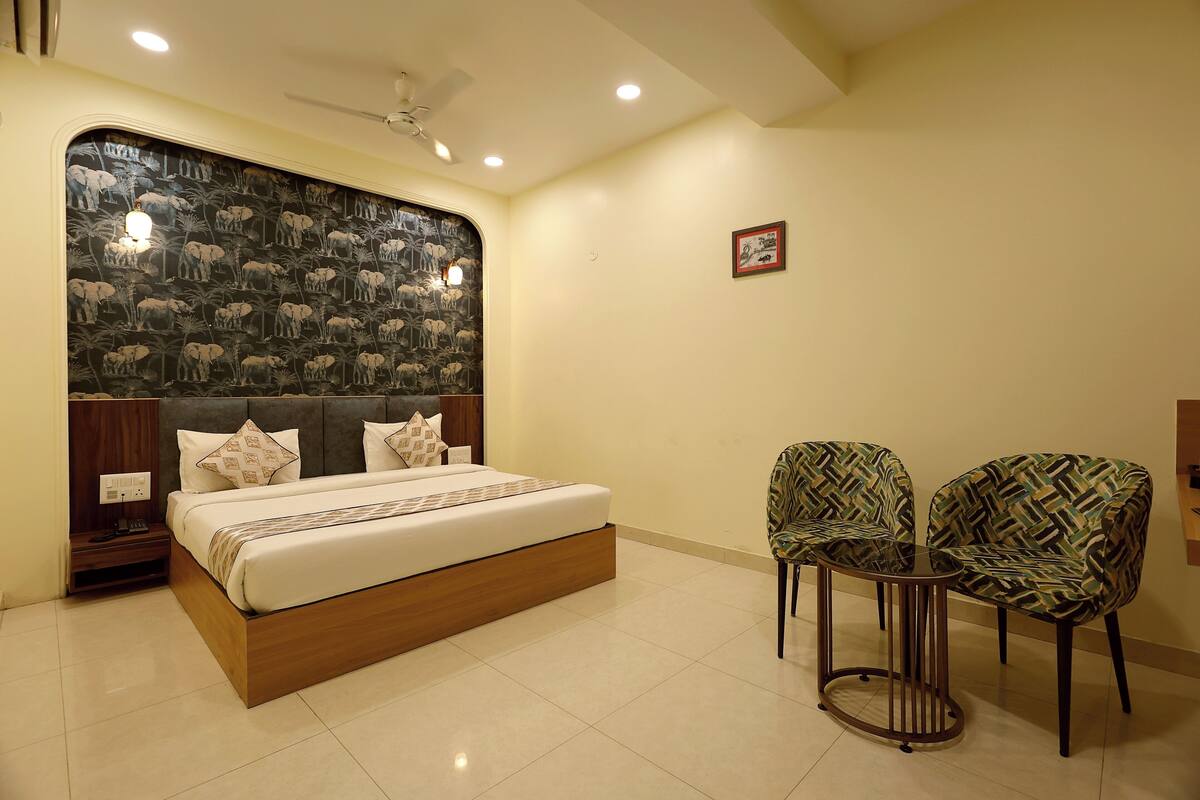 A bedroom with a bed, two chairs, a small table, a ceiling fan, and a wall with a patterned design.