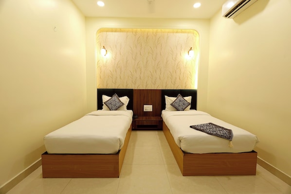 A hotel room with two single beds, a wooden headboard, a wall-mounted light fixture, and a small nightstand. - The Blue Vista Hotel (Greater Noida)