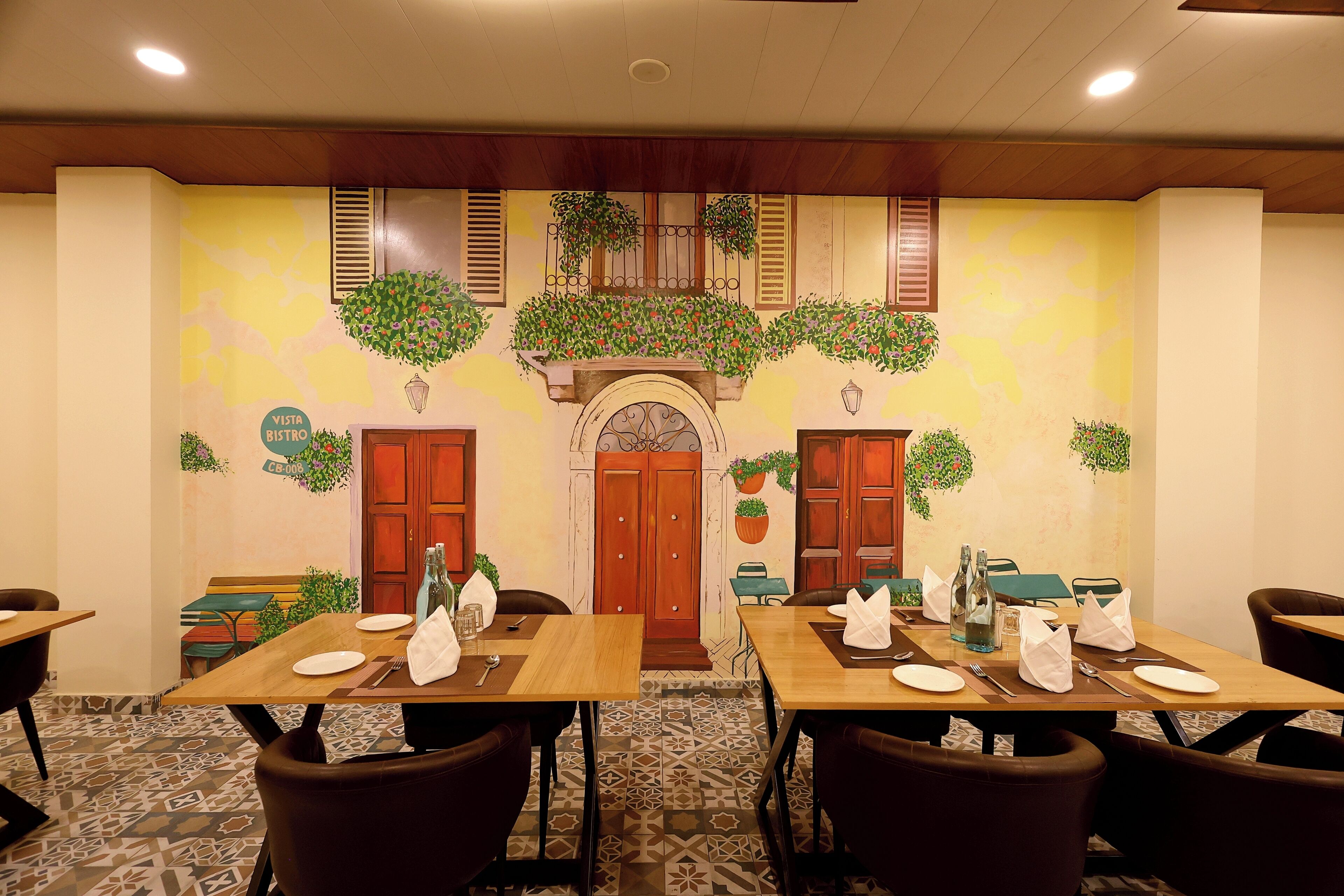 A dining area with tables set for two, wooden chairs, and a decorative wall with plants and a sign that reads "Vista Bistro."