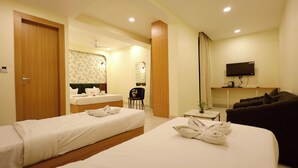 A hotel room with two beds, a sofa, a TV, and a small table. - The Blue Vista Hotel (Greater Noida)