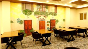 A conference room with multiple tables and chairs, a wooden door, and a wall with hanging plants and a sign that reads "Vista Bistro." - The Blue Vista Hotel (Greater Noida)