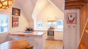 Une cuisine moderne dotée d’un îlot central, d’une cuisinière et d’un évier. De grandes fenêtres laissent entrer la lumière naturelle et des œuvres d’art ornent les murs.