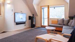 Un salon confortable avec une télévision, une cheminée, un canapé et une grande fenêtre.
