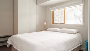 Une chambre à coucher comprenant un lit, une table de chevet, une lampe, une fenêtre et une armoire.