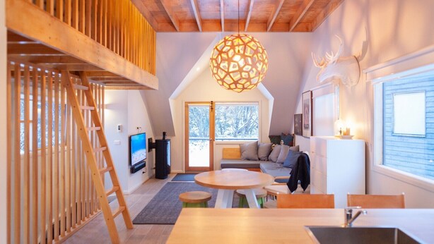 Une pièce chaleureuse de style loft, dotée d’un escalier en bois, d’une table à manger ronde, d’une grande fenêtre donnant sur les arbres et d’un luminaire sphérique original.