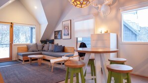 Une pièce chaleureuse et bien éclairée, avec un lit en mezzanine, un canapé, une table à manger et un lustre.