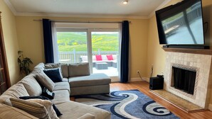 A living room with a beige sofa, a fireplace, and a television mounted on the wall. - 3-bedroom Charming Home in the Hills of Pittsburg with hillside view & pool (Pittsburg)