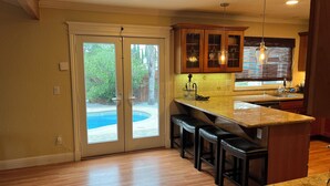 A kitchen with a bar area, wooden cabinets, and a view of a backyard pool. - 3-bedroom Charming Home in the Hills of Pittsburg with hillside view & pool (Pittsburg)