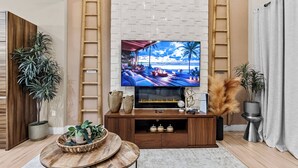 A living room with a large flat-screen TV mounted on a wall, wooden furniture, and decorative plants. - 4BR house with private hot tub in kissimmee (Kissimmee)