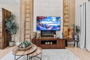 Uma sala de estar com uma televisão de tela grande fixada na parede, mobiliário de madeira e plantas decorativas.
