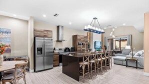 A modern kitchen with a central island, stainless steel appliances, and a dining area with wooden chairs. - 4BR house with private hot tub in kissimmee (Kissimmee)