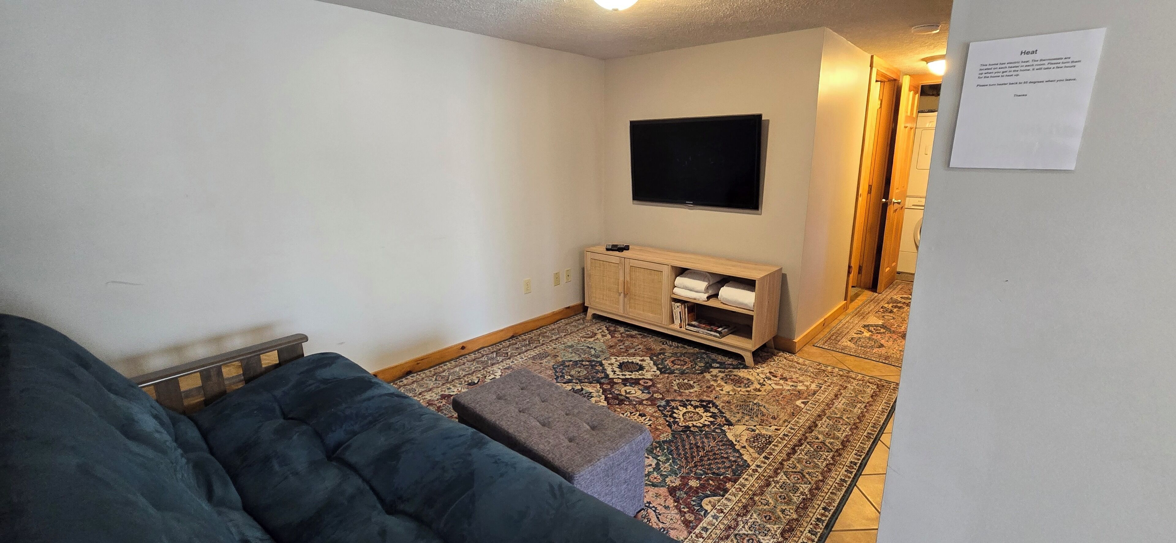 Una sala de estar con sofá, reposapiés, televisor y mueble de almacenamiento.