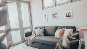 Ein modernes Wohnzimmer mit einem grauen Sofa, einem runden Teppich und gerahmten Kunstwerken an der Wand.