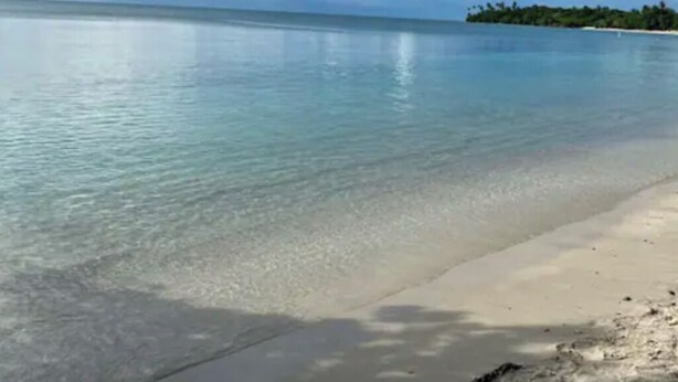 Ein Strand mit klarem, türkisblauem Wasser und sandigem Ufer.