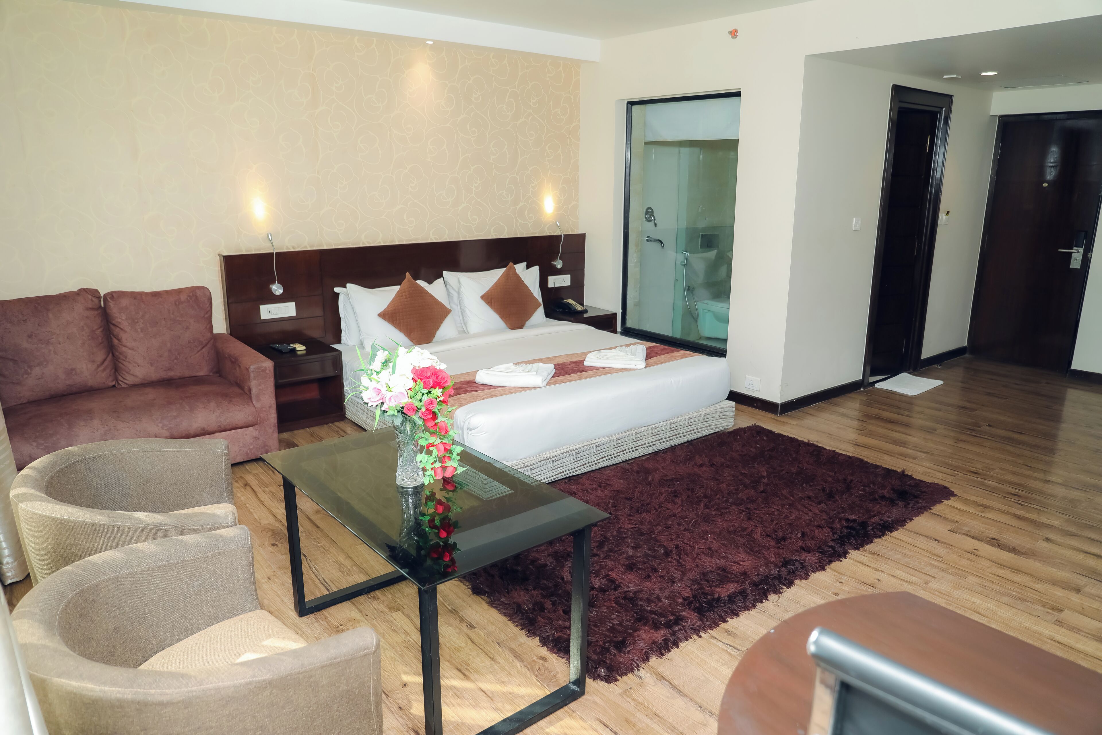 A hotel room with a bed, a sofa, a coffee table, and a glass shower enclosure.
