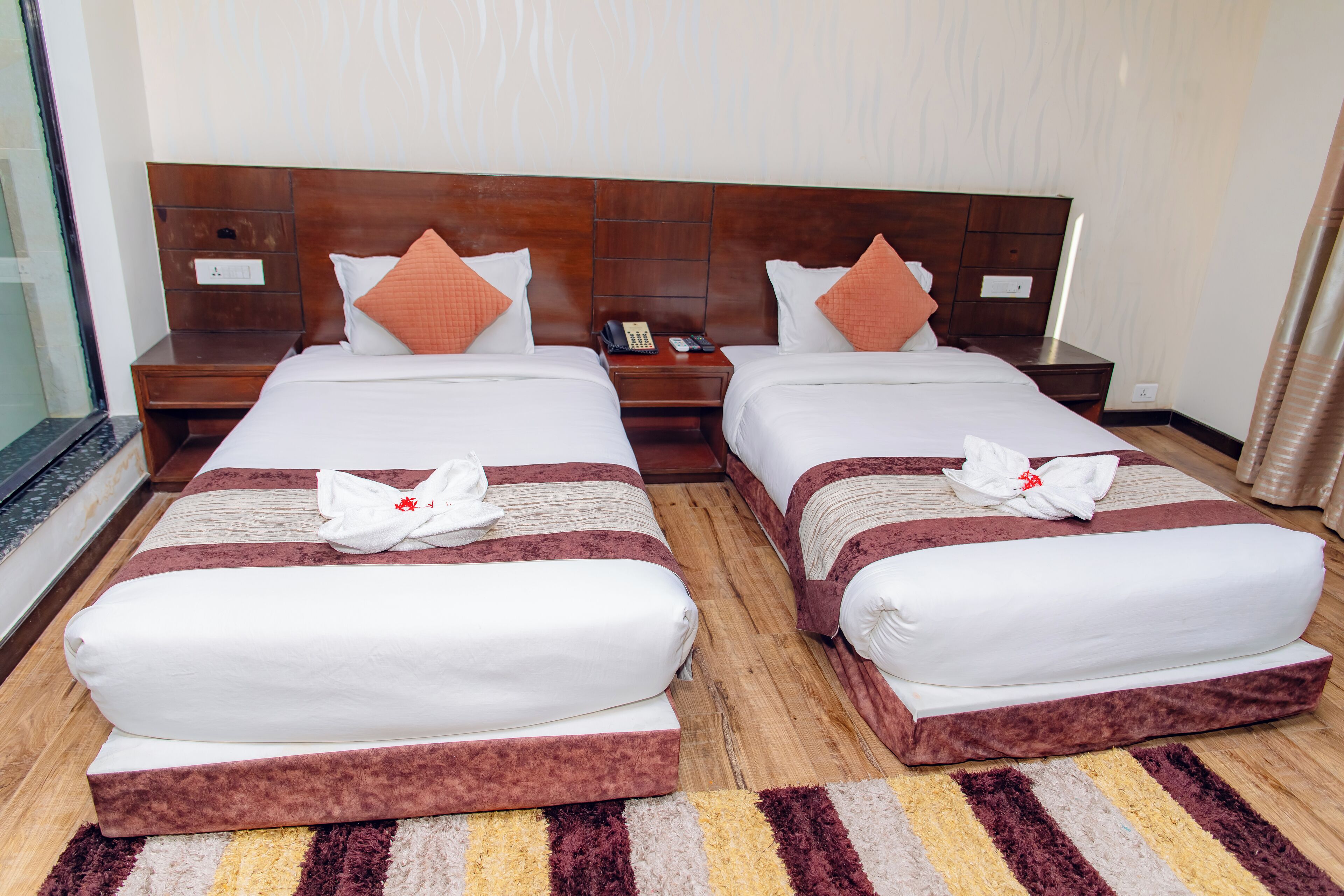 Habitación de hotel con dos camas, cabeceros de madera y un tapete a rayas.
