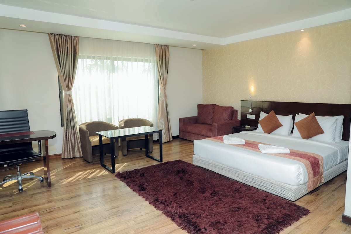 Habitación de hotel con cama, escritorio, silla, televisor y ventana con cortinas.