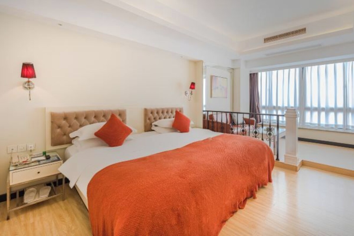 Une chambre d’hôtel avec un grand lit, une table de chevet, une lampe rouge et un balcon doté d’une balustrade.