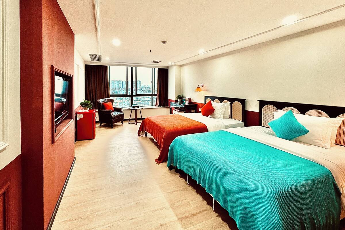 A hotel room with two beds, a TV, a desk, and a window with a city view.