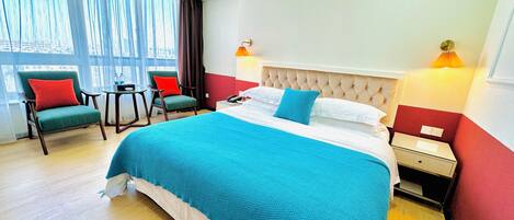 Una habitación de hotel con una cama grande, dos sillas, una mesita pequeña y una mesita de noche.