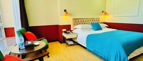 A hotel room with a bed, bedside tables, a small table with a chair, a water bottle, and a tissue box.