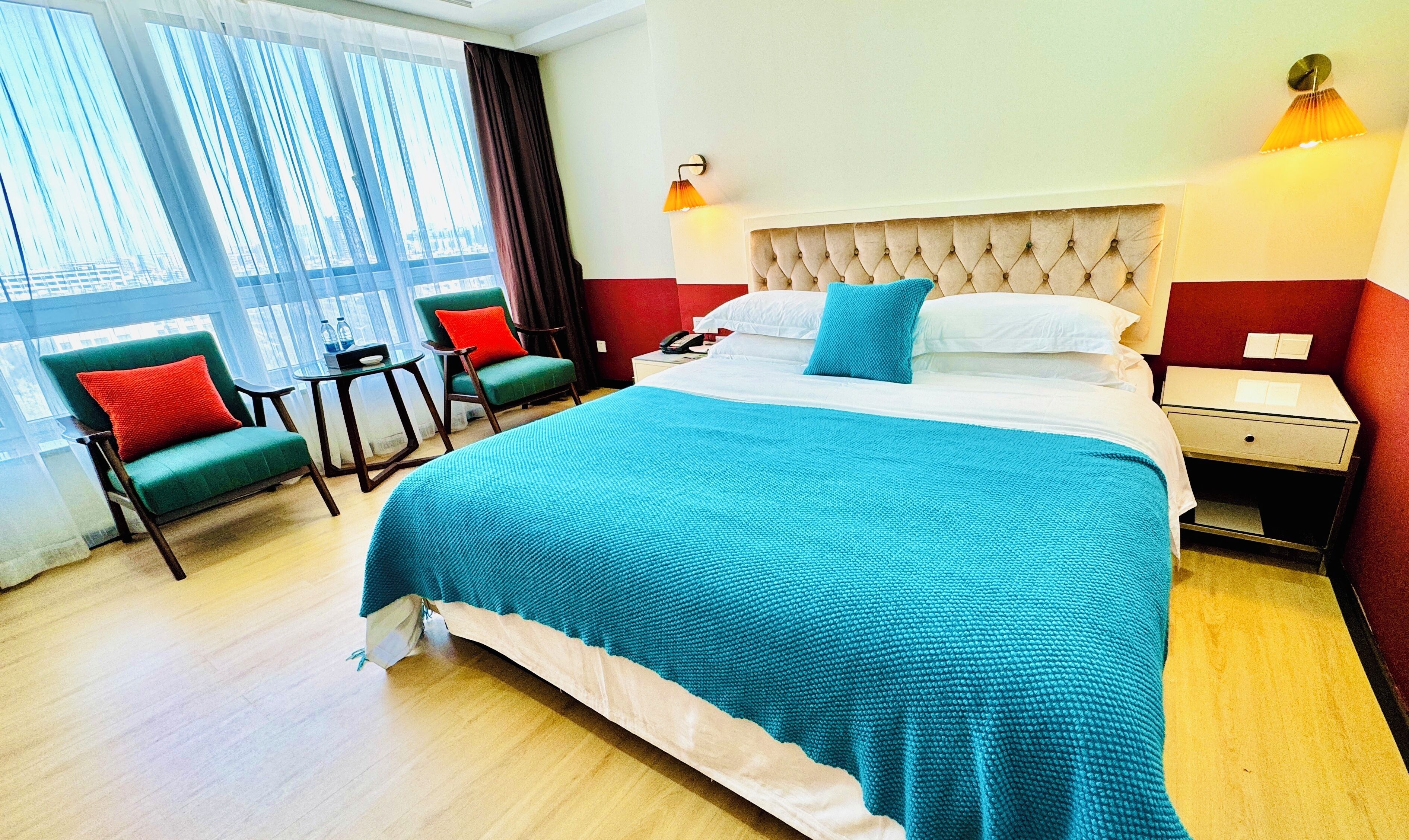 Quarto de hotel com uma cama grande, uma escrivaninha, duas cadeiras e uma janela com cortinas.