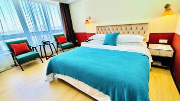 Une chambre d’hôtel avec un grand lit, un bureau, deux chaises et une fenêtre avec des rideaux.