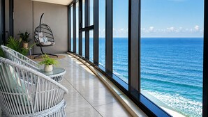 A balcony with a view of the ocean, wicker furniture, and a hanging chair. - Ocean Beachfront Luxe Escape at Surfers Paradise Parking (Surfers Paradise)