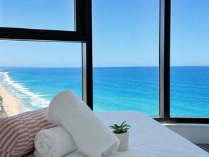 A room with a bed, a window with a view of the ocean, and a small potted plant.
