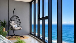 A balcony with a hanging chair, potted plants, and a view of the ocean. - Ocean Beachfront Luxe Escape at Surfers Paradise Parking (Surfers Paradise)