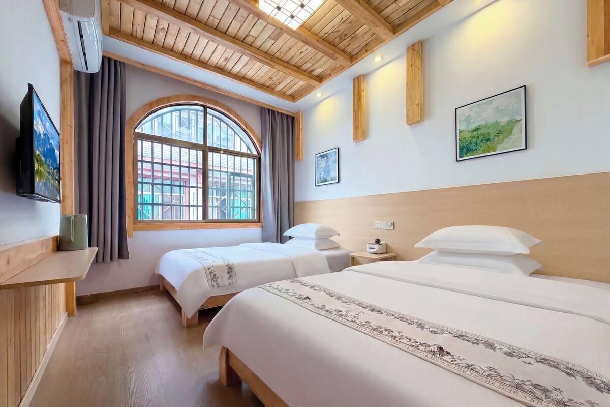 Habitación de hotel con dos camas, televisor, ventana con cortinas y techo de madera.