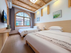 A hotel room with two beds, a TV, a window with curtains, and a wooden ceiling.