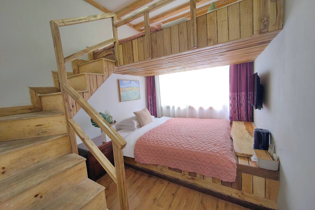 Una habitación con literas, una escalera de madera, una ventana con cortinas y un cuadro en la pared.