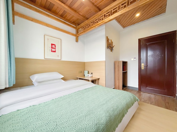 A hotel room with a bed, a wooden headboard, a wall-mounted artwork, a bedside table with a lamp, a wardrobe, and a door with a decorative design. - Just waiting for you (Zhangjiajie)