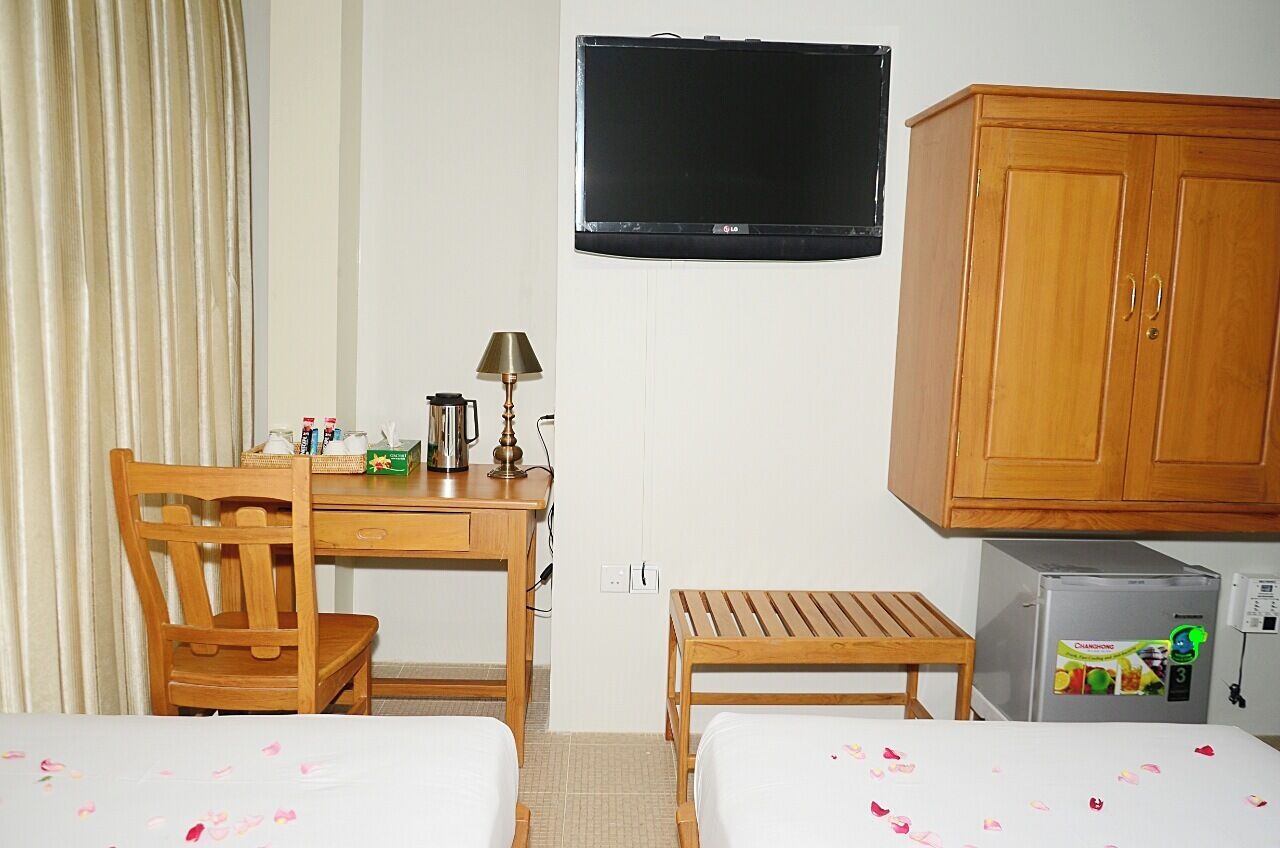 Een hotelkamer met twee bedden, een bureau met lamp, een televisie, een kledingkast en een koelkast.
