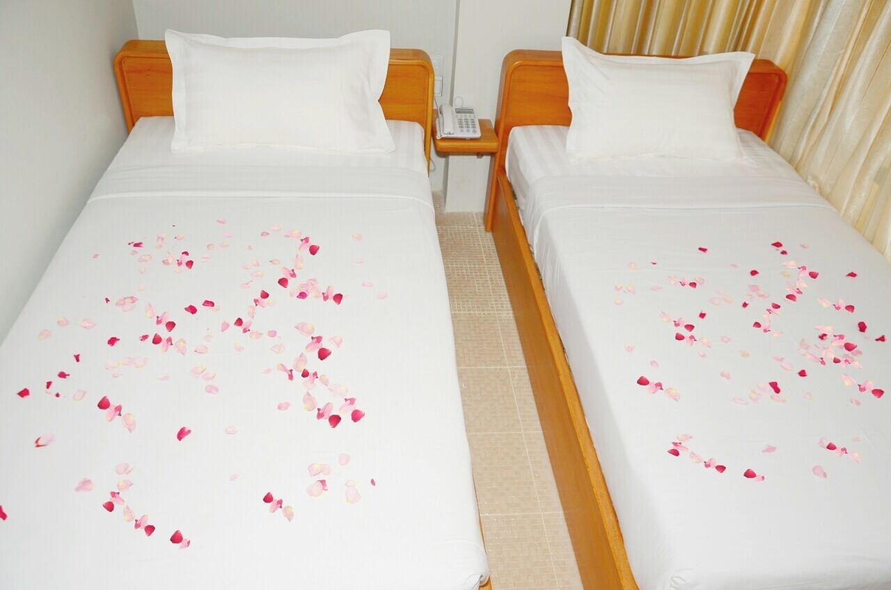 Una habitación de hotel con dos camas individuales, cada una con una colcha blanca y pétalos de rosa esparcidos.