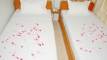 Una habitación de hotel con dos camas individuales, cada una con una colcha blanca y pétalos de rosa esparcidos.