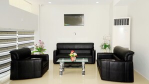 A modern living room with a black leather sofa, a glass coffee table, and two black armchairs. A flat-screen TV is mounted on the wall above the sofa. - Hotel YNO (Yangon)
