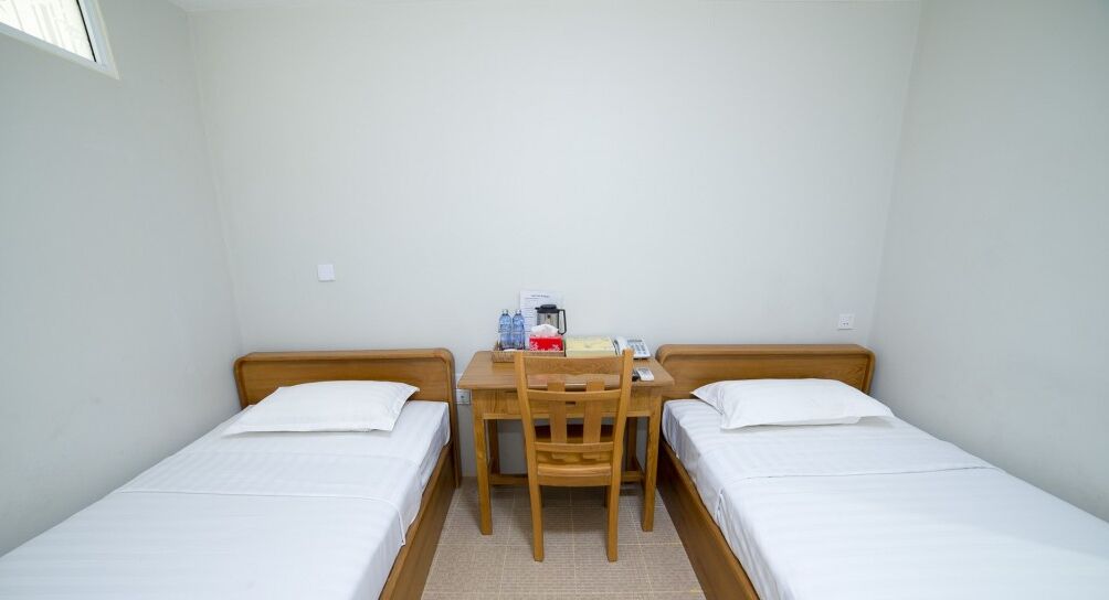 A small, clean room with two single beds, a wooden desk, and a chair.
