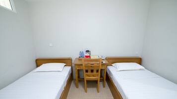 A small, clean room with two single beds, a wooden desk, and a chair.