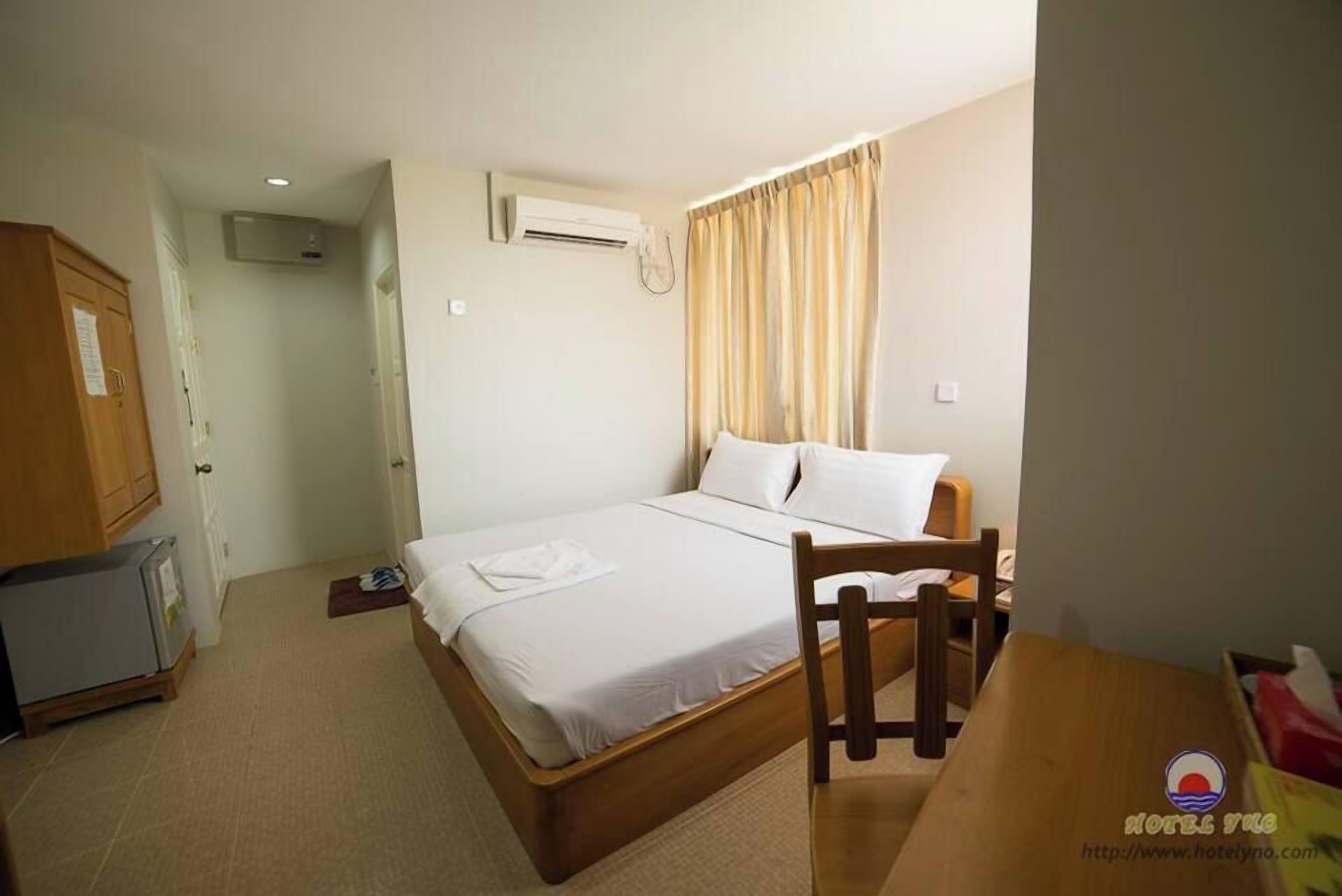 Une petite pièce propre, avec un lit simple, une chaise en bois, une petite table et un appareil de climatisation.
