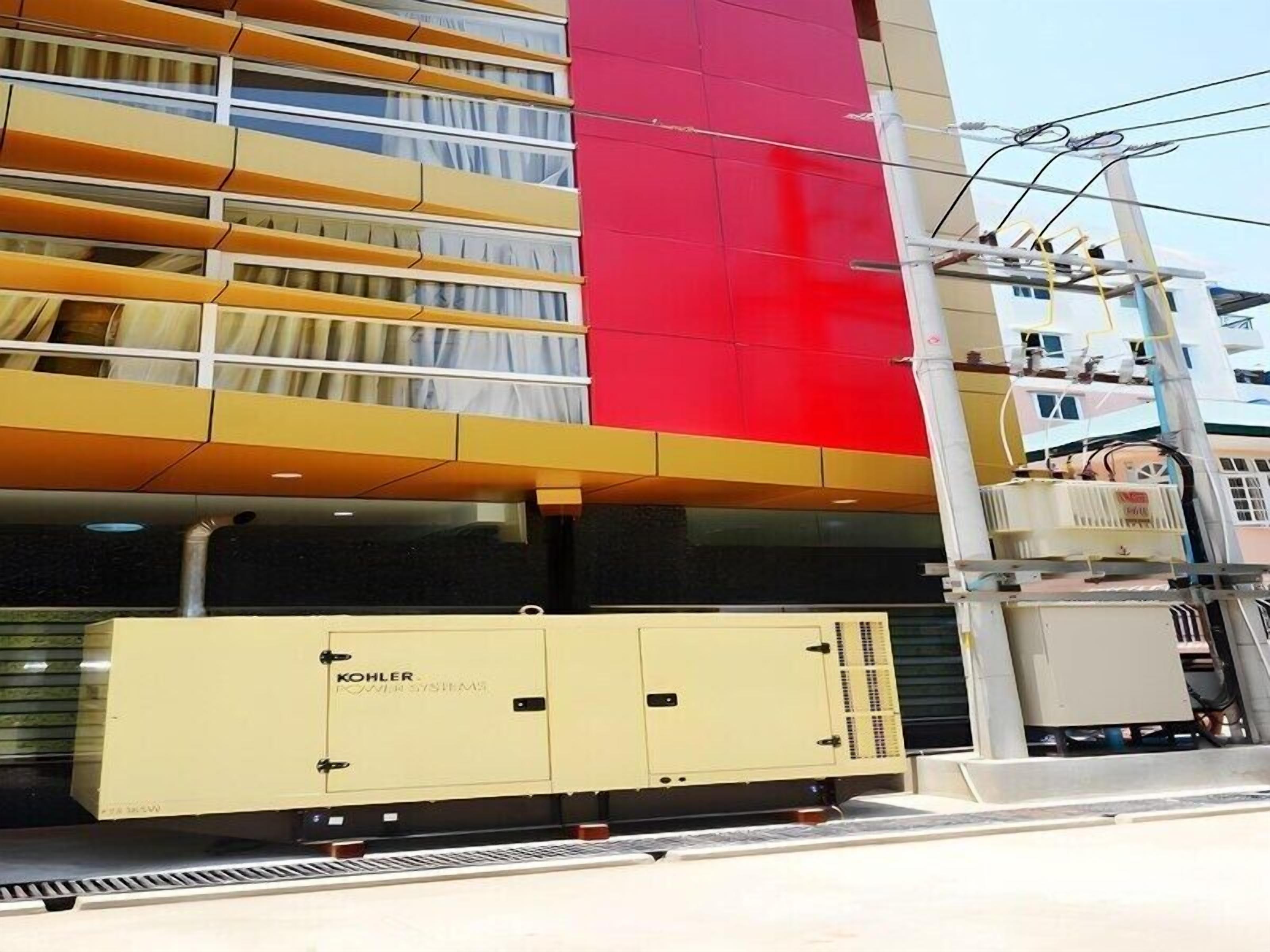 A modern building with a red facade and a large yellow electrical box labeled "Kohler Power Systems" in front.