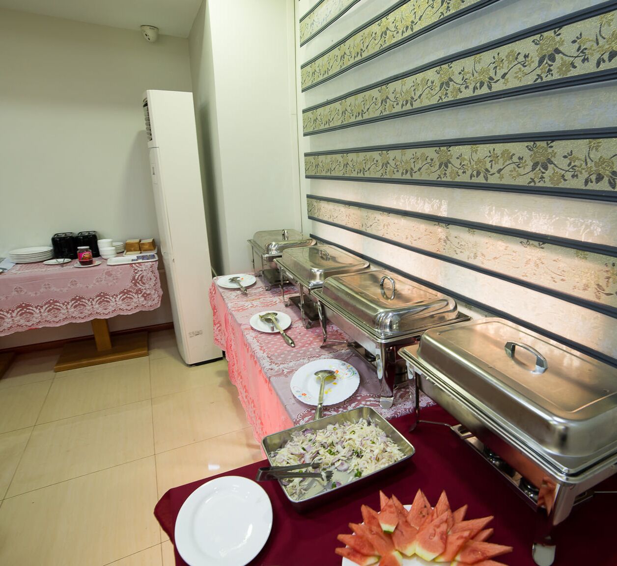 A buffet setup with multiple serving stations, a refrigerator, and a table with a lace tablecloth.