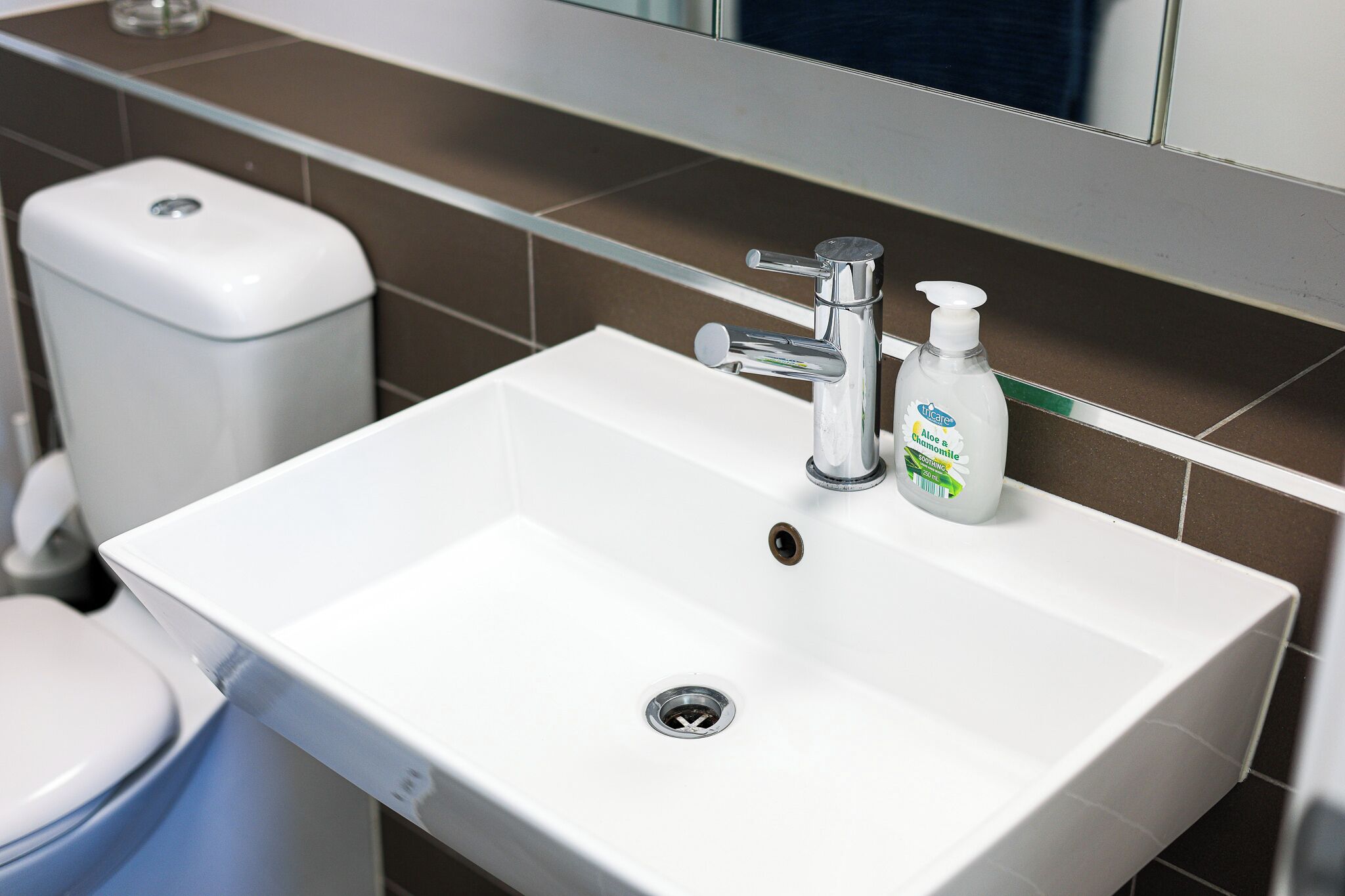 A bathroom with a white sink, a chrome faucet, and a soap dispenser.